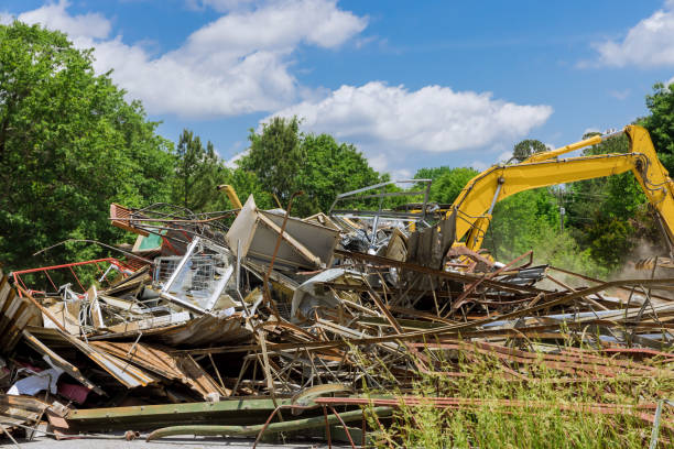 istock Construction equipment demolishes building in clear blue sky with green trees 2185669498