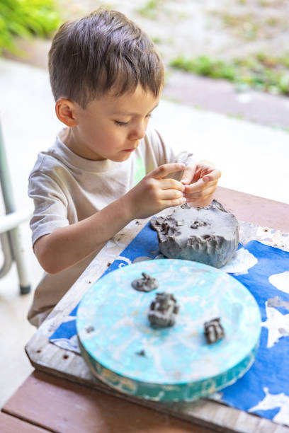 Little boy engaged in clay modeling, creating small sculptures on a wooden table outdoors