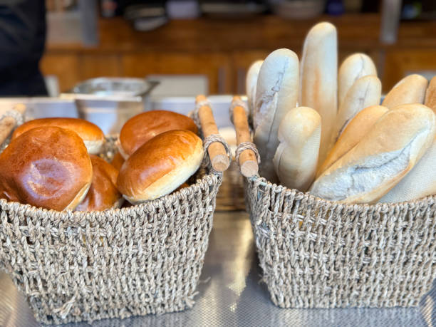 Stock photo showing close-up view of a bakery display counter containing two woven, seagrass bread baskets filled with submarine roll baguettes and glazed bread rolls available for purchasing.
