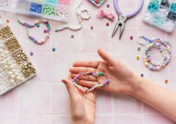 istock Child making beaded bracelets at home on pink tiled table 2185676998