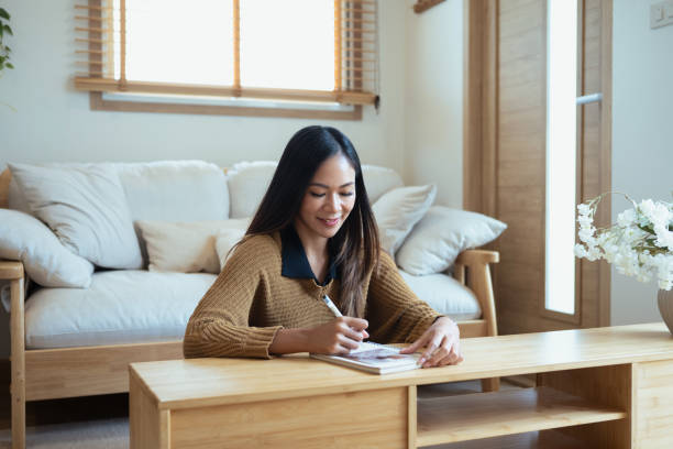 istock Attractive young woman writing notes on a diary while relaxing in a minimalist living room 2185680132