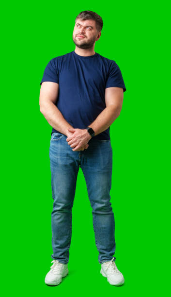 istock Man standing with a thoughtful expression in a casual outfit against a green background 2185680815