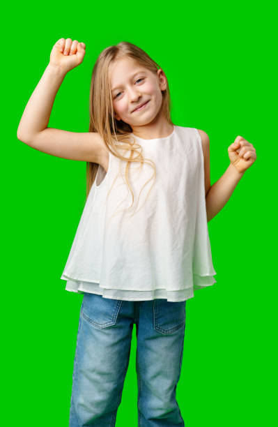 Young girl joyfully dancing with raised arms against a bright green background