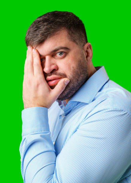 istock A man covers his face with his hands, displaying an expression of surprise or embarrassment against a bright green background 2185682611
