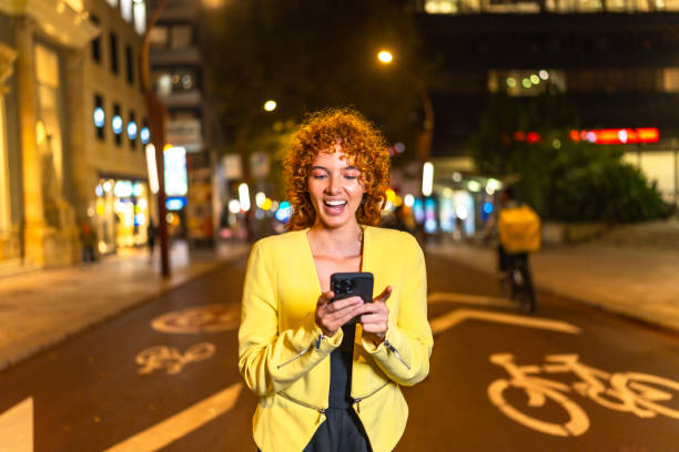 istock Woman expressing surprise while using smartphone at city at night 2185686326