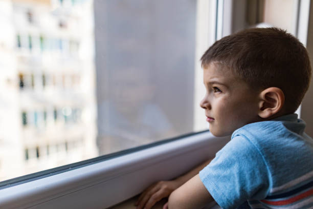 istock Profile view of cute boy looking through window. 2185687841