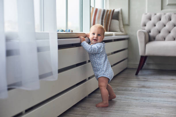istock Baby exploring a bright living room while holding onto the window ledge in the afternoon light 2185694843