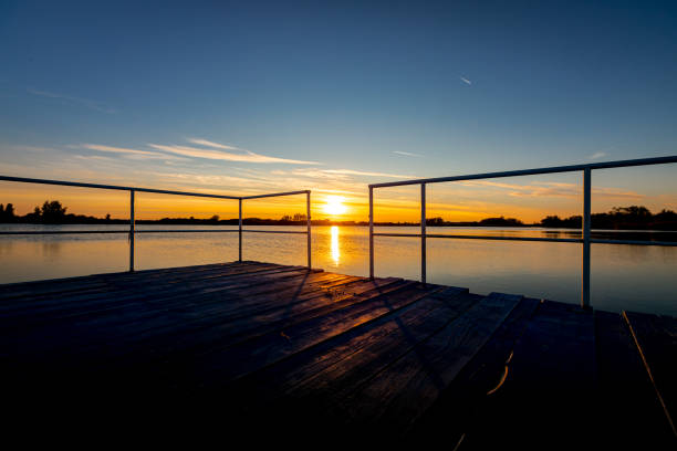 Long exposure shot early in the morning at sunrise on calm lake, sunlight reflecting in water, swimming pier