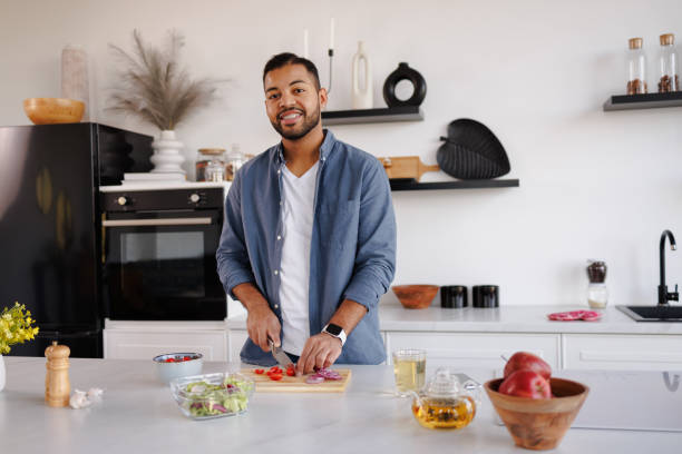 istock Smiling african american man looking at camera while cooking fresh salad in kitchen at home 2185695704