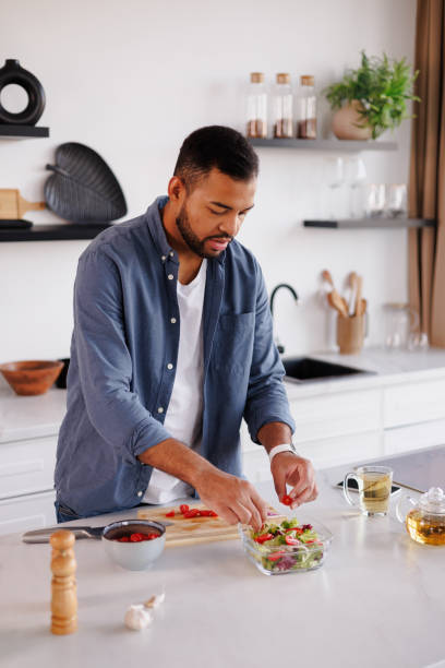 istock African american man adding cherry tomatoes while cooking salad near tea in kitchen 2185695828