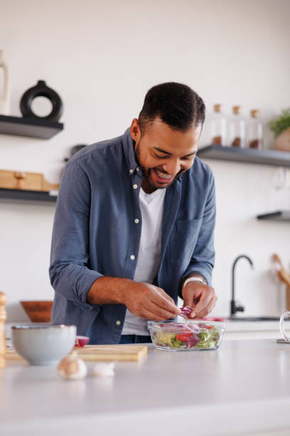 istock Cheerful african american man adding onion in salad in modern kitchen 2185695962