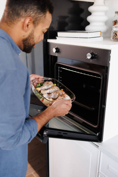 istock Black man putting baking dish with chicken meat in oven while preparing food at home 2185697282