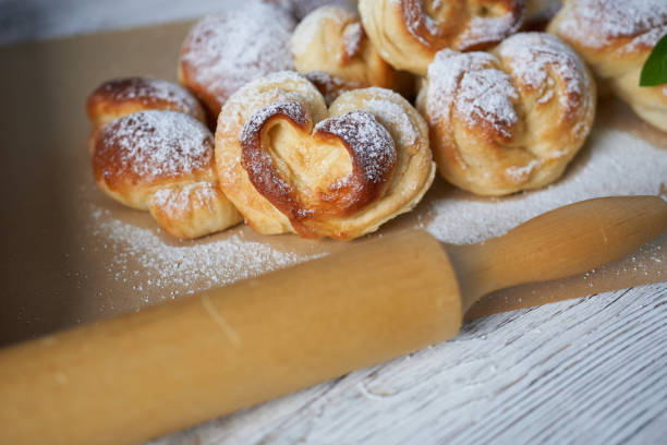 Homemade yeast dough buns with icing sugar and a rolling pin on a wooden table.