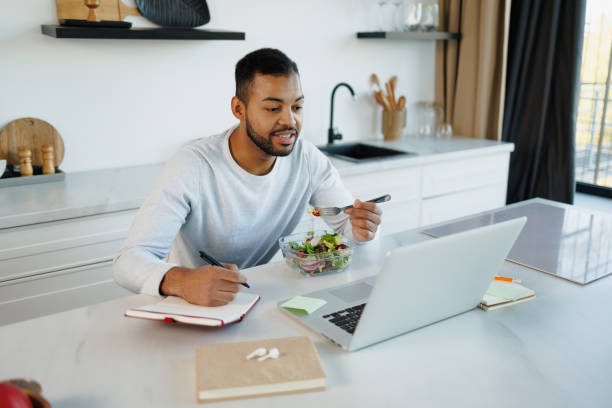 istock African american man writing on notebook and using laptop near fresh salad in kitchen 2185697496