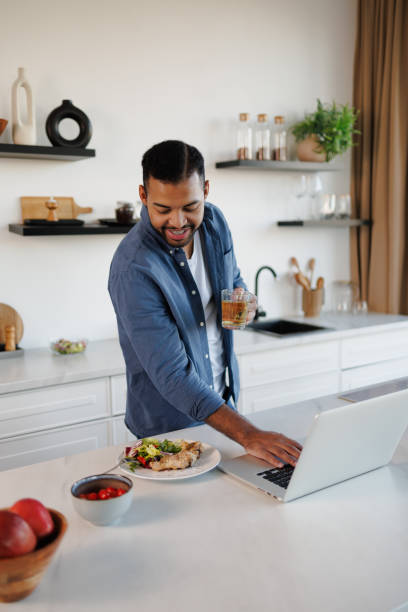 istock Positive african american man holding herbal tea and using laptop near dinner in kitchen 2185697498