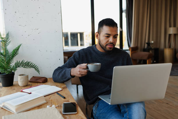 istock African american man holding coffee and using laptop while working at home 2185698664