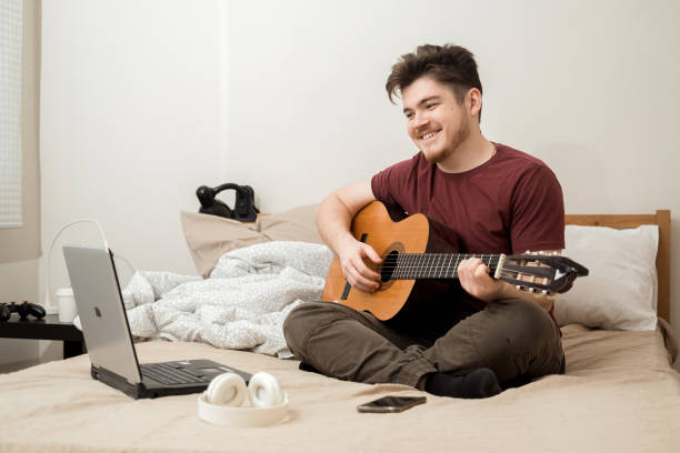 istock A young man learns to play acoustic guitar at home using a computer. 2185701126