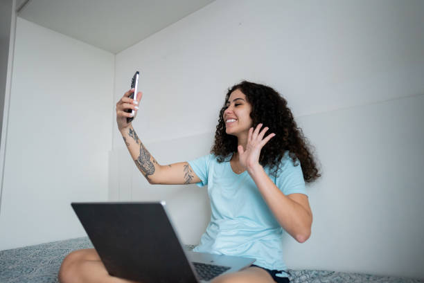 istock Young woman using laptop and making video call with mobile phone at home 2185701649
