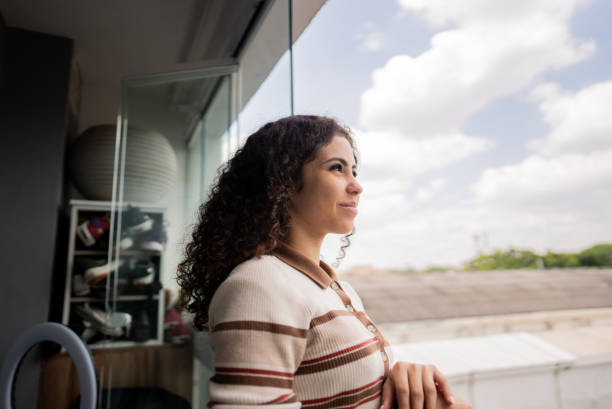 istock Young woman looking through window in apartment 2185702070