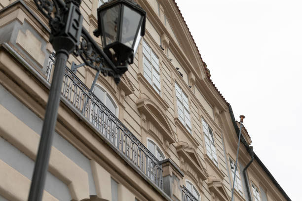 The facade of a historic building with an elegant balcony and beautifully crafted decorative elements, alongside a classic street lamp that is featured prominently in the foreground