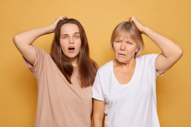 istock Two women with puzzled expressions standing against a yellow background while scratching their heads in confusion, showcasing a moment of disbelief or surprise 2185711197