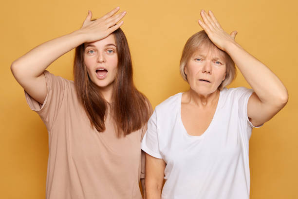istock Two women expressing surprise and confusion against a bright yellow background while holding their foreheads in a playful manner during a casual moment together 2185711206