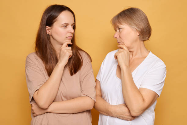 istock Two women with thoughtful expressions engage in a conversation against a bright yellow background, demonstrating contemplation and curiosity about a shared topic 2185711258
