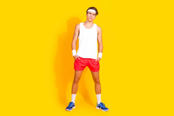 A young, handsome athlete stands confidently in sporty attire against a bright yellow background, exuding health and energy, ready for a workout or sports activity.