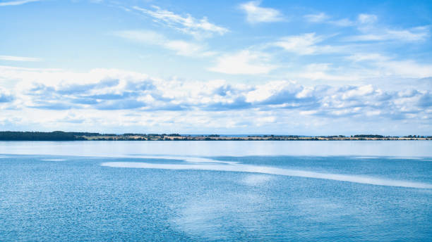 Tranquil seascape under a clear blue sky. The water reflects gentle clouds, while the horizon emphasizes the distance.