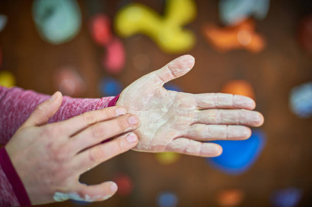 Hands covered in chalk are positioned against a textured wall in an indoor rock climbing gym. A focused climber prepares to tackle climbing routes in a vibrant setting.