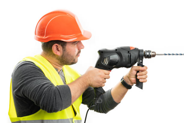 Focused expression male builder frilling hole using electric tool into invisible wall as blank copyspace isolated on white studio background