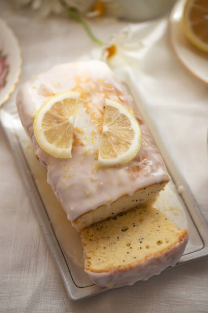 A mouthwatering lemon drizzle cake sits on a wooden plate, beautifully arranged in a cozy kitchen. The natural light highlights the cake's zest, ideal for dessert enthusiasts and tea time moments.