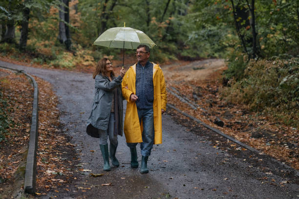 istock Happy embraced senior couple walking with umbrella at forest 2185729043