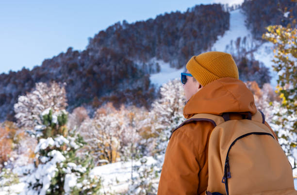 istock rear view of man in red ginger jacket and hat with yellow backpack looking at beautiful mountain view with an autumn winter forest landscape Hiking and tourism 2185734376