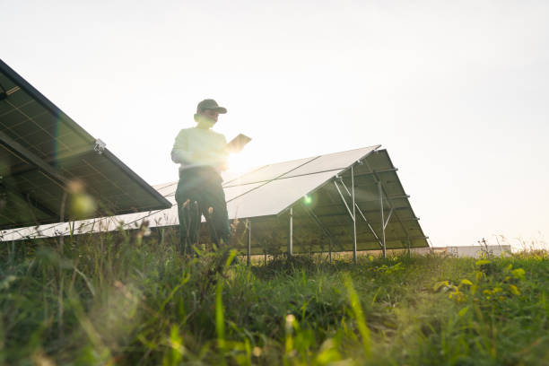 istock Female farmer wearing work uniform holds digital tablet in her hands stands next to solar panels. Modern agricultural farm using solar panels. 2185734406