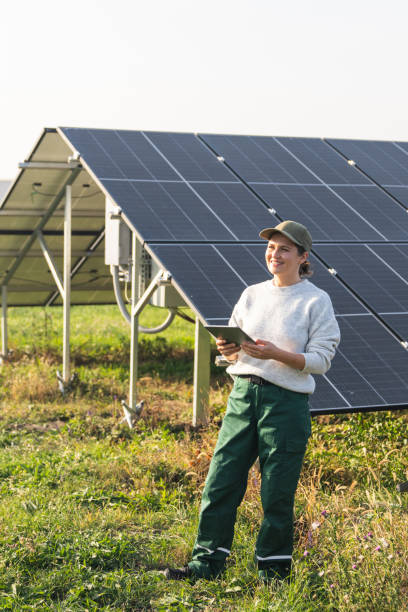 istock Female farmer wearing work uniform holds digital tablet in her hands stands next to solar panels. Modern agricultural farm using solar panels. 2185739100