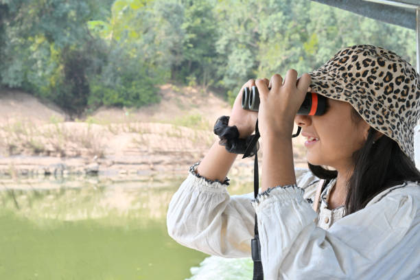 Smiling young woman looking through binoculars near river and rocks in fall season Research of Bird migration Ecologist or wildlife manager Copy space Eco tourism