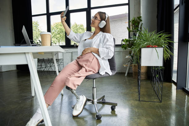 istock Young woman taking a selfie with a prosthetic leg in a modern workspace 2185747076