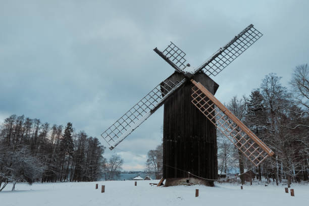 A historic windmill stands tall in a winter landscape in Estonia, surrounded by a blanket of snow and leafless trees. The cloudy sky adds a serene touch to the tranquil scene.