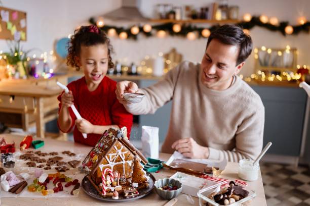 istock Father and daughter decorating a gingerbread house 2185754748