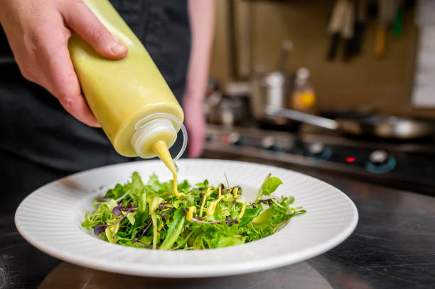 istock A chef’s hands drizzling dressing over a fresh green salad on a white plate, with a blurred kitchen background. Perfect for culinary, cooking, and food preparation themes. 2185756488