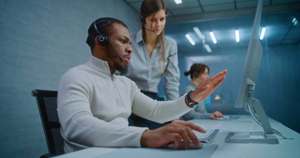 istock Two multiethnic technical support specialists wearing headsets monitoring data on computer 2185759068
