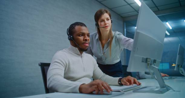 istock Two multiethnic technical support specialists wearing headsets monitoring data on computer 2185759777