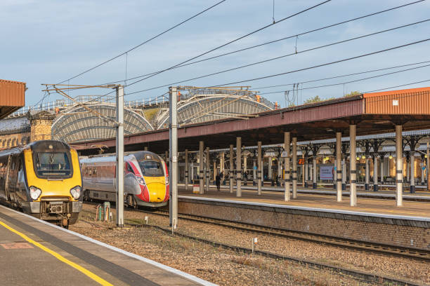 York, UK. November 13, 2024.  Two trains stand at railway platforms waiting to depart. A historic 19th century arch of metal and glass are in the background and workmen are on the walkway.