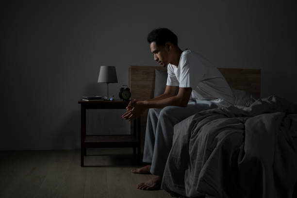 depressed young asian man sitting in bed, struggling with insomnia and unable to sleep. - 1人 夜 ストックフォトと画像