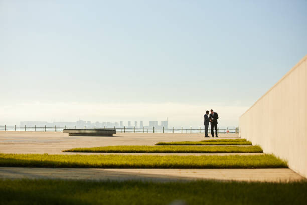 Two business professionals discussing plans on modern rooftop with city skyline in background and expansive empty space allowing for potential text or design elements