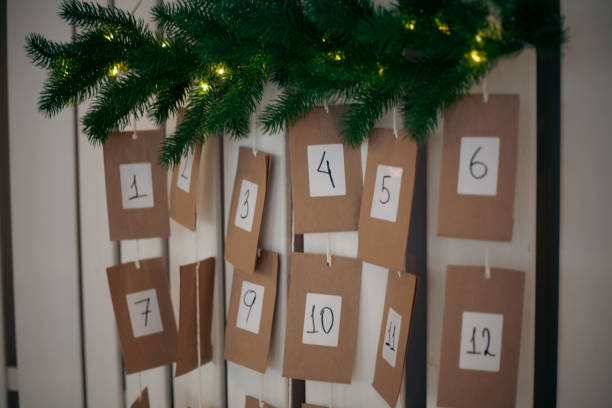 istock Decorative advent calendar mounted on a wall features numbered kraft cards from one to twelve, enhanced with a garland of greenery and small lights, indicating holiday anticipation 2185764562