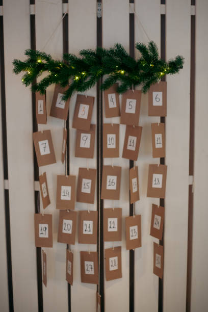 istock Hanging advent calendar features numbered brown cards arranged in a decorative pattern on a wall with green foliage and fairy lights above, creating a festive atmosphere for the holiday season 2185764563