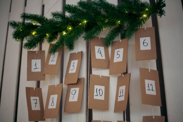 A festive advent calendar is showcased against a wall, with numbered pockets hanging from strings, illuminated by soft fairy lights and accented with fresh greenery