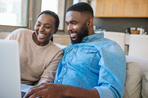 istock Laughing African American couple using a laptop on their sofa 2185766628